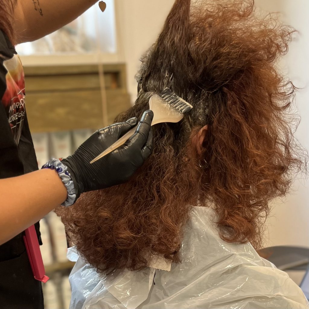 Parrucchiera che applica una tinta ai capelli ricci di una donna
