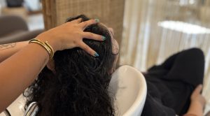 Parrucchiera che massaggia la testa di una donna con capelli lunghi ricci scuri