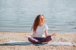 Donna con capelli ricci rossi fa yoga sulla spiaggia