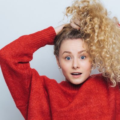 Ragazza che si lega i capelli lunghi ricci biondi con un elastico