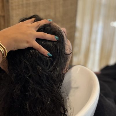 Parrucchiera che massaggia la testa di una donna con capelli lunghi ricci scuri