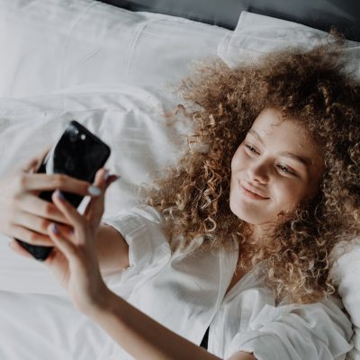 Donna con capelli ricci lunghi stesa sul letto che si fa un selfie