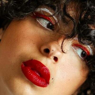 Donna con capelli ricci, trucco occhi rosso e bianco, labbra rosse