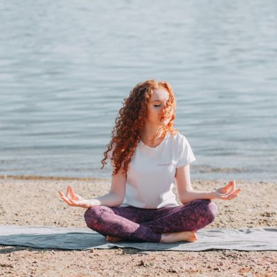Donna con capelli ricci rossi fa yoga sulla spiaggia