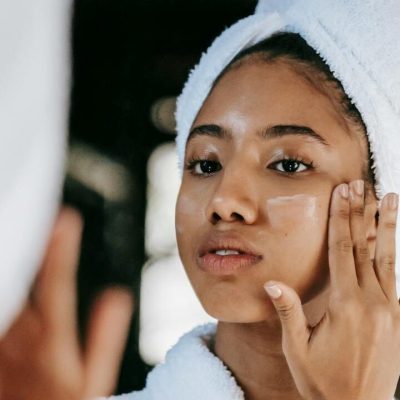 Donna con asciugamano in testa applica crema idratante sul viso